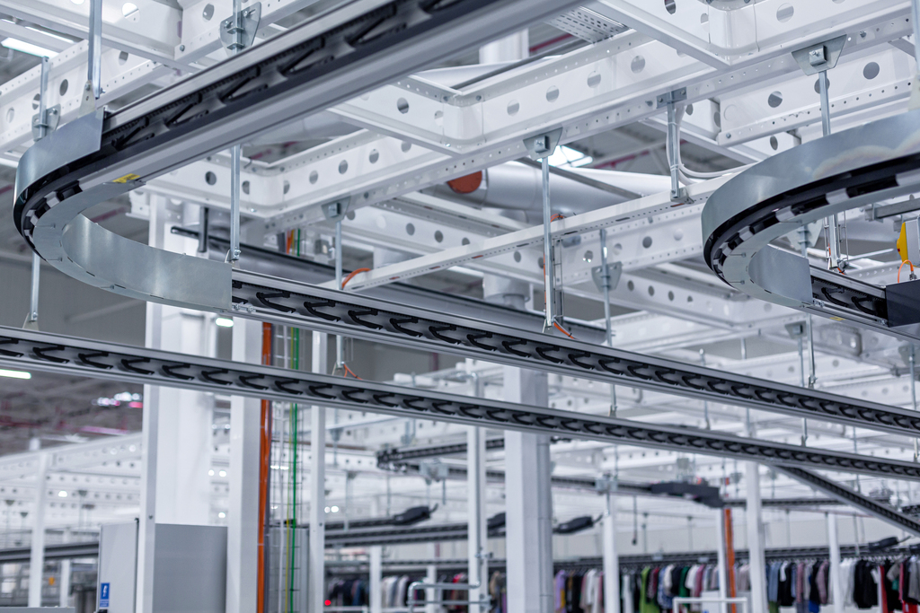 Empty overhead garment conveyor system installed in a warehouse, showing rail structure and layout.