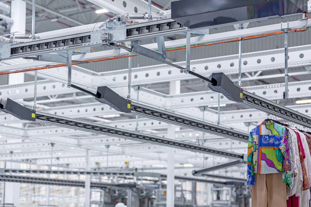 Parallel garment conveyor lines in a warehouse, with one line carrying garments on hangers and others empty.