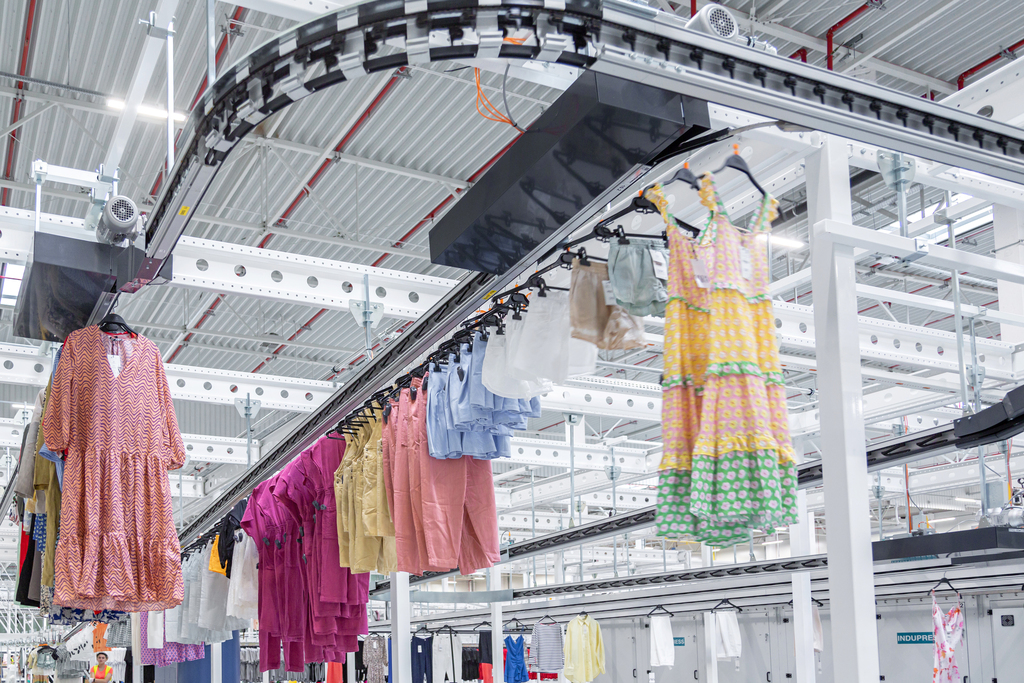 Colorful garments on hangers transported across a multi-level garment handling conveyor system in a warehouse.